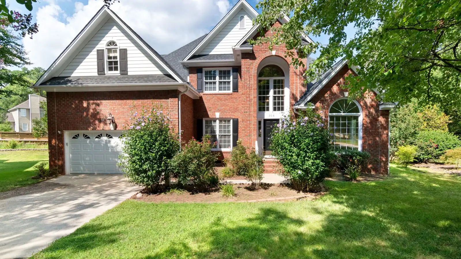 Two-story brick house with a green front lawn on a sunny day