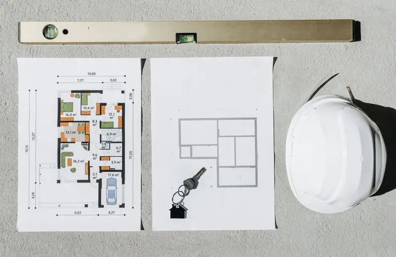 Spirit level, house plans and a hard hat on a table